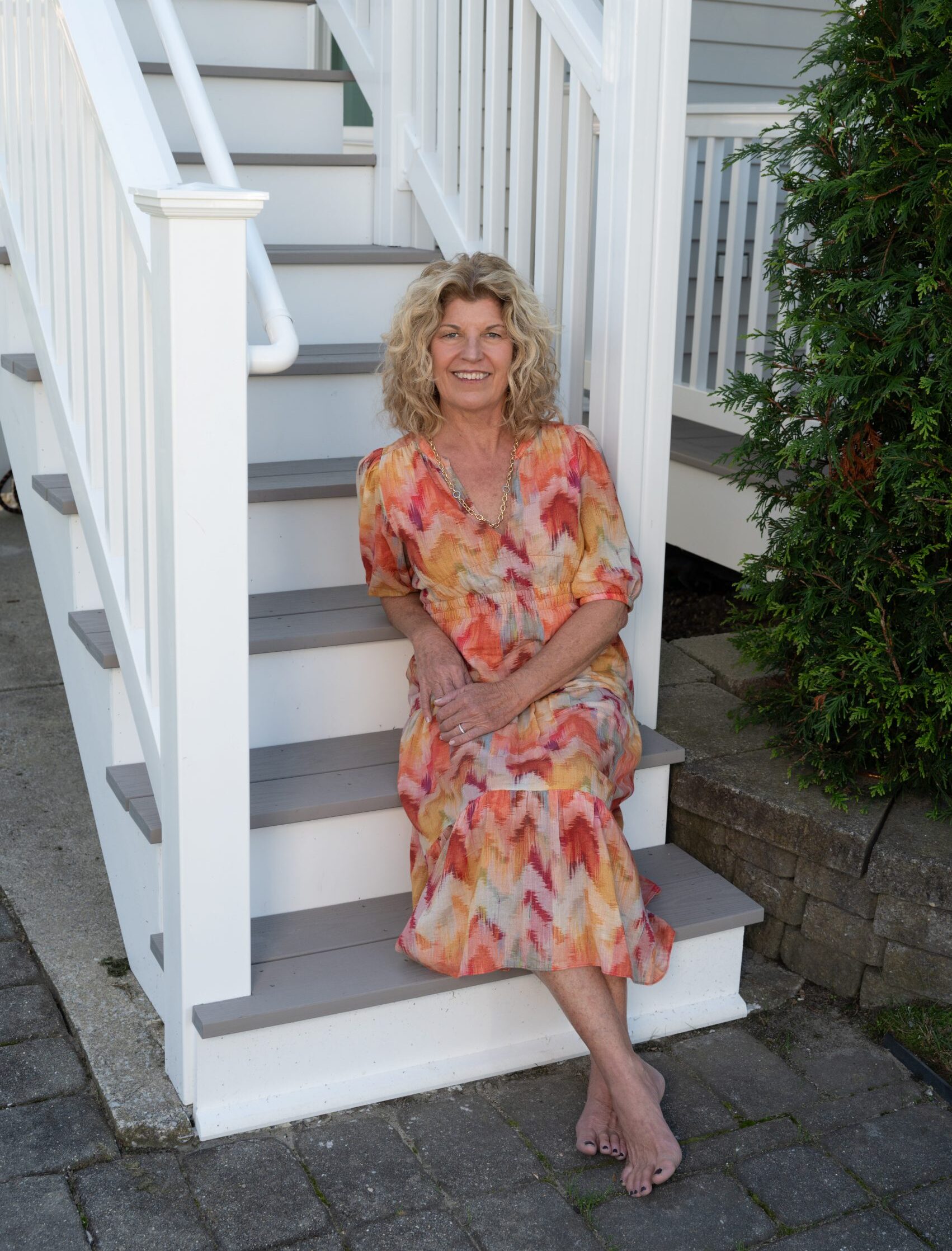 Laura Bishop seated on a staircase with a colorful dress on.